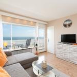 Living room with sofa, TV, and sea view through large windows.