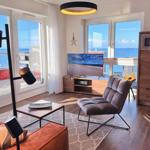 Wohnzimmer mit Meerblick, Sofa, Sessel und Fernseher.