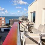 Terrasse mit Sitzgelegenheiten und Meerblick. Rote Balustrade, moderne Möbel.