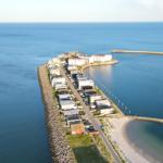 Aerielansicht einer Küstenstadt mit Häusern, Straße und Strand.