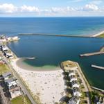 Aerielansicht eines Hafens mit Strand, Bootshäfen und Wohnhäusern an der Küste.