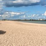Strand mit Sand, Strandkörben und Häusern am Horizont unter bewölktem Himmel.