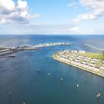 Aerial view of coastal town with marina, houses, and sea under partly cloudy sky.