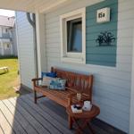Deck with wooden bench, table, and drinks in front of a house with blue siding and round door window.