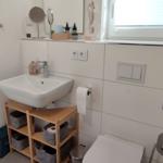 Bathroom with sink, toilet, and shower. Wooden shelf under the sink.