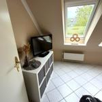 Dachgeschosszimmer mit TV, Fenster und Fliesenboden.