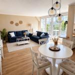 Wohnzimmer mit Essbereich, blauer Couch, weißen Stühlen und Holzboden.