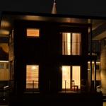 Moderne Holzhütte mit beleuchteten Fenstern und Außenterrasse bei Nacht.