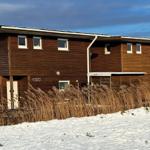 Holzhaus am Wasser mit Schnee und hohem Schilf.