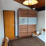 Bedroom with bed, wardrobe, and door. Wooden ceiling and nightstand with lamp.