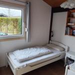 A bedroom with a white bed, window, and bookshelf.