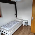 A bedroom with a white bed, nightstand, and wooden floor.