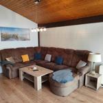 A living room with a brown sofa, wooden floor, and wooden ceiling. There is a coffee table and a table lamp.