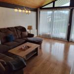 A living room with a brown sofa, wooden floor, and large windows with white curtains.
