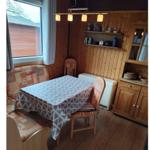 Dining room with wooden walls, table, chairs, and window. Tablecloth is on the table.