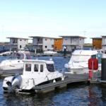 Hafen mit Booten und modernen Steg-Häusern im Hintergrund.