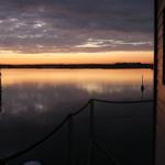 Sonnenuntergang über ruhigem Wasser mit Blick von einem Bootssteg.