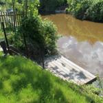 Holzsteg führt zum Wasser. Grünflächen und Bäume umgeben den Fluss.