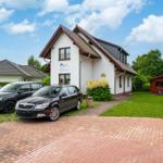 Haus mit gepflastertem Hof, Grünfläche und mehreren parkenden Autos.