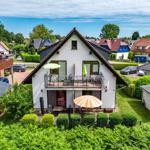 Ein zweistöckiges Haus mit Balkon und Garten. Ein orangefarbener Sonnenschirm steht im Vorgarten.