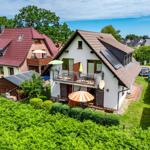 Wohnhaus mit Balkon, Garten und Sonnenschirmen. Umgeben von grüner Vegetation.
