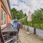 Terrasse mit Tisch, Stühlen, Sonnenschirm und Liegestuhl neben rotem Backsteinhaus.