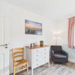 Ein Raum mit Stuhl, Schrank, Sessel und Fenster mit Vorhängen.
