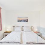 Zimmer mit Doppelbett, zwei Nachttischen und Wandbild. Vorhang mit Streifen.