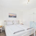 Schlafzimmer mit Doppelbett, weißen Schränken und Wandbild. Holzfußboden und Nachttische.