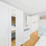 Schlafzimmer mit weißem Schrank und Bett. Holzboden und Wandbild.