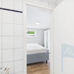Schlafzimmer mit Bett, Fenster und Holzboden. Tür zum Bad mit Fliesenwand.