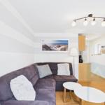 Ein Wohnzimmer mit einem grauen Sofa, zwei weißen Kissen und zwei runden Tischen.