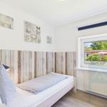 A bedroom with a bed, wooden wall, and window overlooking the garden.