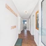 Hallway with wooden floor, coat rack, and door to the bathroom.