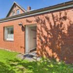 Red brick house with entrance and window. Grass area in front of the wall.