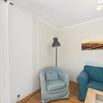 A room with a light blue armchair, a teal sofa, and wall decor.