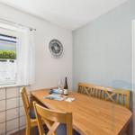 Dining room with wooden table, chairs, and wall clock. Window with curtain. Door to hallway.