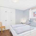 Bedroom with white bed, wardrobe, and window.