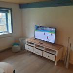 Wohnzimmer mit Fernseher, Holz-TV-Schrank und Fenster mit blauem Rahmen.