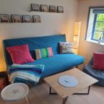 Blauer Schlafsofa mit Kissen und Decke, Holztisch, Sessel und Fenster mit Blick auf Grün.