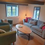 Wohnzimmer mit Sofa, zwei Sesseln und ovalen Tisch. Holzboden und Fenster mit Blick.