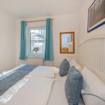 Schlafzimmer mit Bett, Fenster, Vorhängen und Wandbildern.