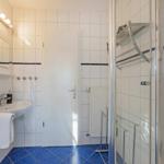 Badezimmer mit Dusche, Waschbecken und Spiegel. Fliesenboden und weiße Wände.