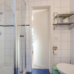 Badezimmer mit Dusche, Toilette und Handtuchhalter. Weiße Fliesen und blaue Bodenfliesen.