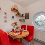Rundes Fenster, rote Stühle, Holztisch, Wandregale mit Dekoration.
