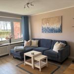 Ein Wohnzimmer mit blauem Sofa, Tisch und Wandbild. Fenster mit Vorhängen.