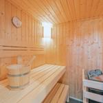 Sauna mit Holzbank, Eimer und Thermometer an der Wand.