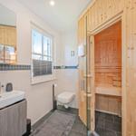 Badezimmer mit Sauna, Waschbecken und Toilette. Holzverkleidung und Fenster sichtbar.