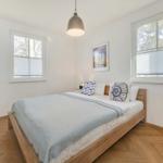 Schlafzimmer mit Holzbett, Fenstern und Wand-TV.
