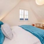 Schlafzimmer mit Dachschrägen, Bett mit blauer Decke, Fenster und Fernseher.